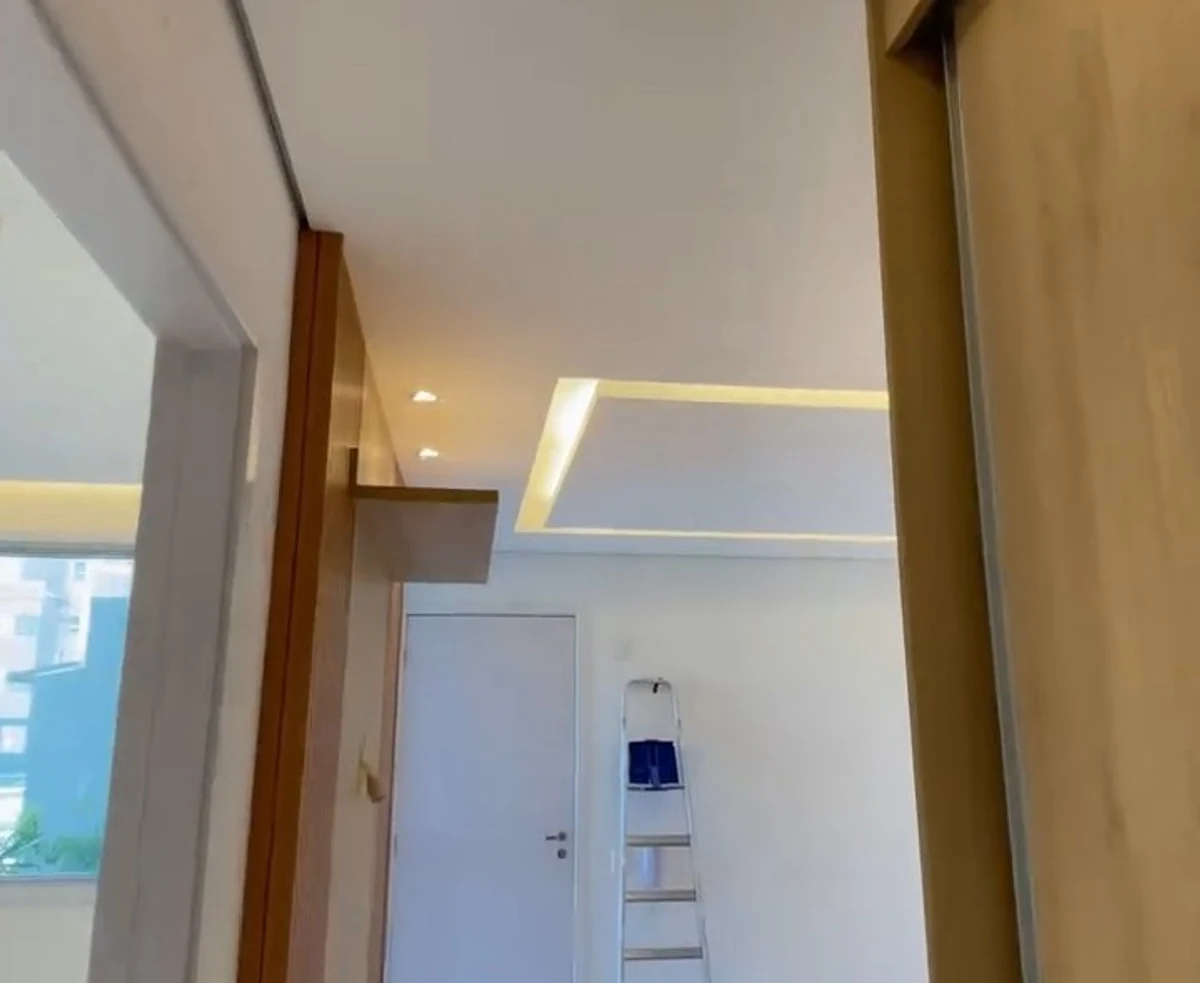 Corredor com forro rebaixado e iluminação linear embutida acompanhando o caminho.